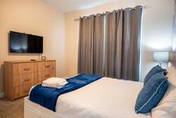 Rest in a cozy bedroom with a clean white bed, blue accent throw, wood headboard, geometric feature wall, soft lamps, gray curtains, and warm natural details, creating a comfortable space for vacation.