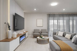 Relax in a bright and stylish living room with a cozy gray sectional, wall-mounted TV, elegant chairs, soft curtains, and warm wood accents. The neutral decor and natural light create a calm space for family vacation moments.