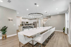 Gather in a bright dining area with a long white table, modern chairs, elegant ring lights, soft curtains, warm wood flooring, and open access to the kitchen.