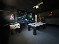 Enjoy a dark space themed game room with a pool table, foosball, arcade machine, projector setup, cue rack, and bold galaxy mural, perfect for games and entertainment.