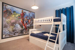 This vibrant kids' bedroom with a cozy bunk bed and a superhero mural ignites imagination. Plush carpeting and deep blue curtains create a warm atmosphere, making it the ideal place for rest after a day filled with adventure.
