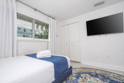 Enjoy a bright, airy bedroom featuring a plush bed with crisp linens and a stylish blue throw, all enhanced by large windows that fill the space with natural light, creating a serene atmosphere for a relaxing stay.