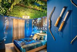 Rest in an Avatar themed bedroom with a cozy bed, blue walls, leafy ceiling, glowing lights, bold wall art, and bow-and-arrow decor, creating a fun space for vacation.