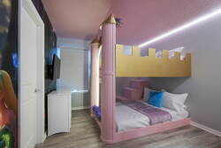 This whimsical kids' room is bright and playful, featuring a charming castle-themed bunk bed, cozy pink bedding, modern lighting, and a stylish TV, creating the perfect spot for relaxation after exciting adventures.