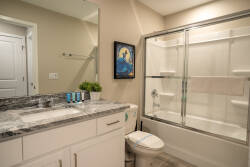 Enjoy the comfort of this beautifully designed bathroom with sleek granite countertops and a spacious glass shower. Soft lighting highlights the light, neutral tones, while a vibrant piece of art adds a unique touch to the space.