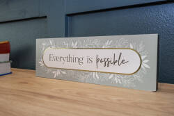 A charming decorative sign on a warm wooden surface radiates positivity with its vibrant colors and floral accents, adding character and a welcoming vibe that invites you to embrace the possibilities of your stay.
