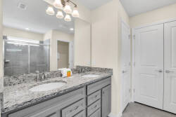 Enjoy the charm of this stylish bathroom with a dual sink vanity, sleek granite countertops, and modern gray cabinetry. The illuminated mirrors add brightness, creating a welcoming atmosphere for your stay.
