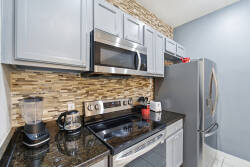 Welcome to a stylish kitchen with gray cabinetry and a beautiful stone backsplash. Modern stainless-steel appliances, including a spacious refrigerator and microwave, create an inviting space for your culinary adventures.