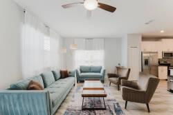 Bright and airy, this living room features a plush teal sofa paired with stylish armchairs, creating a cozy spot for relaxation. Natural light floods through large windows, enhancing the soft, inviting textures of the space.