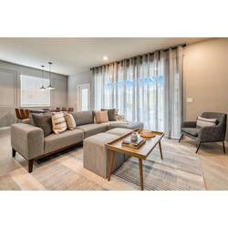 Experience a cozy living area with plush gray furnishings and a stylish coffee table, ideal for relaxing after your adventures. Large windows with soft curtains let in natural light, creating a warm and inviting ambiance.