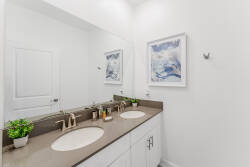 This bright bathroom boasts a sleek double vanity with smooth stone countertops and elegant fixtures, enhanced by calming artwork. The clean lines and natural light create a refreshing atmosphere for your morning routine.