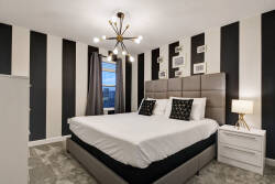 Experience a stylish bedroom with bold black and white striped walls, a plush king-sized bed with chic pillows, a contemporary light fixture, and a large window that fills the space with natural light for an inviting ambiance.