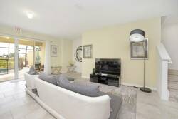 This bright living room boasts a spacious white sofa with textured gray pillows, inviting relaxation. Large sliding doors flood the space with natural light and provide a lovely view of the outdoors, creating a cozy ambiance.