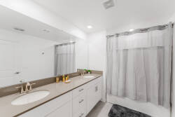 Experience a bright and clean bathroom featuring dual sinks and a spacious vanity, perfect for your morning routine. The sleek countertops and soft gray curtains create a calming atmosphere, enhancing your stay.