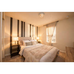 Rest in a warm bedroom with a cozy white bed, striped accent wall, soft lamps, beige curtains, neutral carpet, and calming decor for vacation comfort.