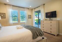 Bathe in natural light in this cozy bedroom, featuring a plush bed adorned with a soft throw and a stylish dresser. Enjoy the serene view through sliding glass doors that lead to an outdoor space, perfect for relaxation.