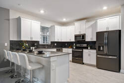 Experience a culinary haven with sleek white cabinetry and a striking dark backsplash, creating a fresh, polished atmosphere. The spacious island with stylish bar stools is perfect for casual gatherings and entertaining.