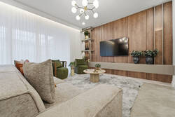 Relax in a stylish living room with a cozy sectional, green accent chairs, wall-mounted TV, warm wood feature wall, soft white curtains, modern lighting, and elegant decor for vacation moments.