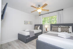 This bright bedroom features two comfortable beds with sleek gray frames, accented by soft textiles and inviting decorative pillows. Natural light streams in through the window, creating a warm atmosphere ideal for relaxation.