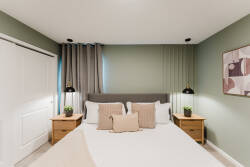 This cozy bedroom, with its soothing green walls and stylish bedside lamps, offers a calming atmosphere. Soft natural light filters through the curtains, creating an inviting space perfect for a restful night's sleep.