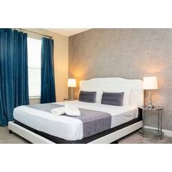 Rest in a stylish bedroom with a comfortable bed, white bedding, gray accents, blue curtains, bedside lamps, textured accent wall, soft carpet, and warm modern decor.