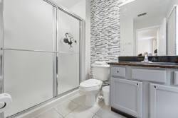 This elegant bathroom boasts a sleek glass shower and a stylish stone accent wall, adding sophistication. The dark granite countertop beautifully contrasts with soft white cabinetry, creating a refreshing atmosphere for your stay.