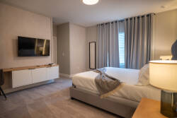 This serene bedroom, adorned in soft neutral tones, offers a calming atmosphere with elegant floor-to-ceiling curtains. Enjoy the comfort of modern furnishings and a sleek mounted TV for your convenience during your stay.