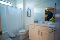 Experience a bright, airy bathroom with a clean, minimalist design, featuring soft beige cabinetry, a spacious vanity, and natural light streaming through the frosted window, all enhanced by a fresh white shower curtain and.