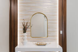 Welcome to a stylish entryway featuring warm wood accents and a chic arch-framed mirror that reflects soft lighting. A sleek white console table holds a decorative bowl and elegant florals, enhancing the inviting atmosphere.