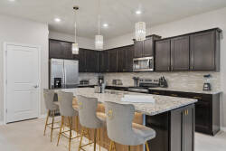 Cook and gather in a stylish fully equipped kitchen with dark cabinets, stainless steel appliances, granite countertops, elegant pendant lights, and a large island with seating, perfect for meals and family moments.