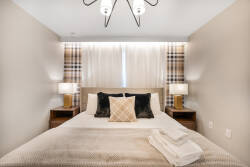 This cozy bedroom offers a plush bed with stylish throws and pillows, warm wood nightstands, and soft bedside lighting, all enhanced by chic patterned curtains that create a calming and sophisticated atmosphere.
