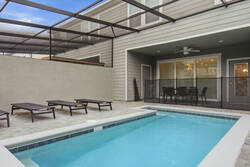 Relax in a private screened pool area with clear blue water, lounge chairs, paved deck, privacy walls, and open sky views, creating a refreshing space for family vacation moments.