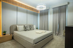 Relax in this stylish bedroom, where a chic chandelier casts a soft glow over plush carpeting and textured wall panels. The calming colors and elegant window treatments create a serene space for your restful nights.