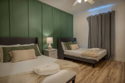 Enjoy restful nights in this beautifully designed bedroom with two comfy beds dressed in soft linens. The rich green accent wall adds sophistication, and natural light through elegant curtains creates a warm, inviting atmosphere.