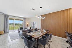 Gather in a bright open dining and living area with a set table, soft gray seating, warm wood accent wall, modern lighting, and sliding glass doors with peaceful balcony views.