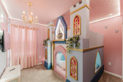Welcome to a whimsical children's bedroom with a vibrant castle bed and soft pink walls that spark imagination. Elegant drapery and a stylish chandelier enhance the charm, creating a perfect setting for delightful adventures.