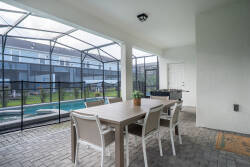 Step onto the screened patio featuring a stylish wooden dining table and modern chairs, where you can enjoy tranquil views of the private pool surrounded by lush greenery, ideal for relaxation and outdoor dining.
