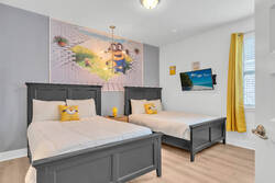 Sleep in a fun Minions themed bedroom with two cozy beds, bright yellow accents, themed pillows, a wall-mounted TV, cheerful wall art, and natural light for a playful family stay.