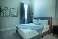 Enjoy the soothing natural light that fills your room, highlighting the plush bedding and calming gray decor. Stylish artwork adds personality, creating a tranquil haven perfect for your relaxation.
