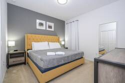 Welcome to this cozy bedroom with a plush yellow upholstered headboard that adds a cheerful vibe. Soft gray walls and inviting linens create a warm atmosphere, while framed art adds charm for a restful night's sleep.
