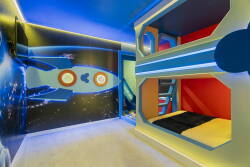 This vibrant kids' room features a fun rocket mural that sparks imagination, while cozy, colorful bunk beds offer a playful and comfortable space for rest, complemented by soft lighting that creates a cheerful bedtime atmosphere.