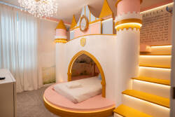 Step into a whimsical bedroom featuring a castle-themed sleeping nook, complete with vibrant pink and yellow accents. Soft, plush carpeting and sheer white curtains create a cozy atmosphere, perfect for a dreamy night’s rest.