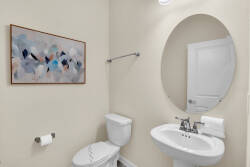 This bright bathroom showcases a sleek oval mirror above a modern sink, with soft neutral wall tones. A colorful abstract artwork adds personality, creating a space that is both functional and stylish for your comfort.