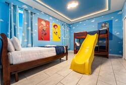 Sleep in a bright Toy Story themed bedroom with blue cloud walls, character posters, cozy beds, a yellow slide, and soft ceiling lighting, creating a fun space for kids.
