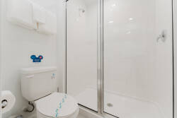 Experience a bright, modern bathroom with sleek white tiles and a spacious glass shower designed for relaxation. Enjoy plush towels and a playful accent, blending comfort and style for your perfect stay.