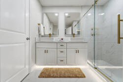 Experience a stylish bathroom with sleek white cabinetry and elegant gold fixtures for a sophisticated touch. The spacious walk-in shower with glass doors invites relaxation, while the plush rug adds warmth and comfort underfoot.