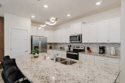 Step into a beautifully designed kitchen featuring sleek white cabinetry and a spacious granite island, perfect for meal prep or casual dining. The modern lighting adds a warm glow, making this space ideal for culinary creativity.