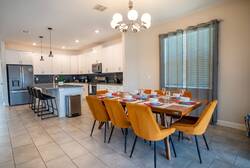 Gather in a bright dining area with a wooden table, orange cushioned chairs, elegant place settings, modern chandelier, soft curtains, and an open kitchen view, perfect for family meals during vacation.